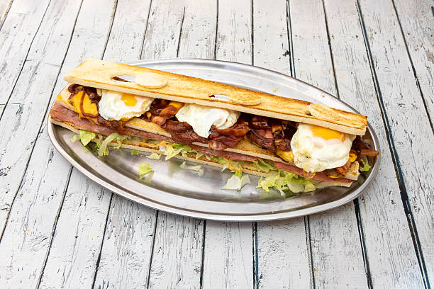 huge ham sandwich with fried eggs, lots of fried bacon slices, cheddar cheese and lettuce and grilled sliced bread