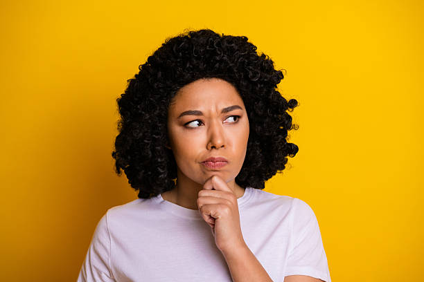 istock Young woman with expressive thoughtful gesture posing against vibrant yellow background wearing casual white shirt 2239746499