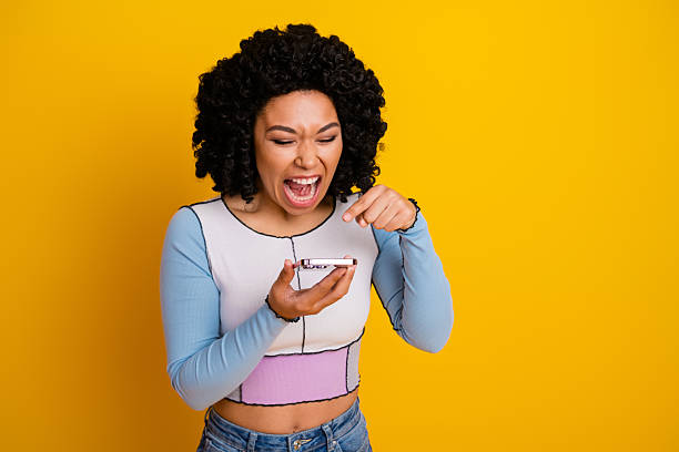 istock Joyful young woman using a smartphone while smiling and pointing on a vibrant yellow background 2239746662
