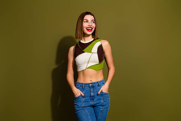 istock Charming young woman in stylish crop top posing confidently against a green backdrop while enjoying a casual relaxed moment 2239748087