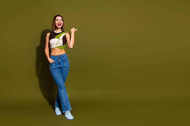 istock Charming young woman smiling and gesturing against solid khaki background, wearing trendy casual outfit and jeans 2239748102