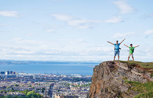 istock Excited hikers revel in panoramic cityscape from a high cliff 2239751379