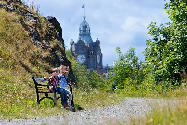 istock Kids wave from park bench with scenic views and a clock tower 2239751402