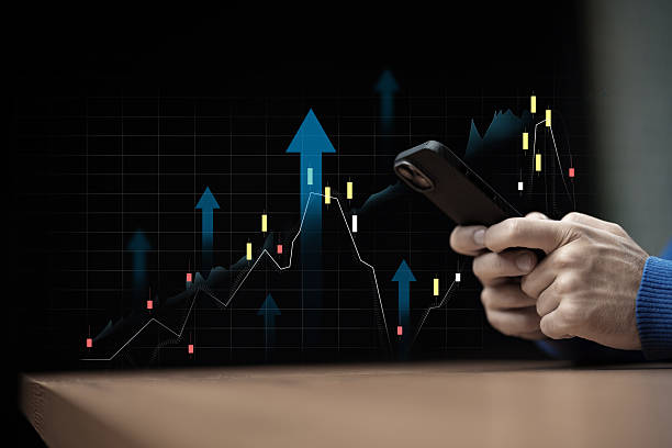Active trader analyzes market trends using smartphone in a dark setting Trader looks at stock market data on smartphone amid colorful trend lines and arrows. best market trading platform stock pictures, royalty-free photos & images