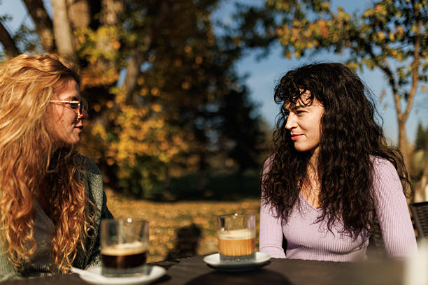 istock Two friends enjoying a lively conversation over coffee outdoors in a park surrounded by autumn foliage on a sunny day 2239754379