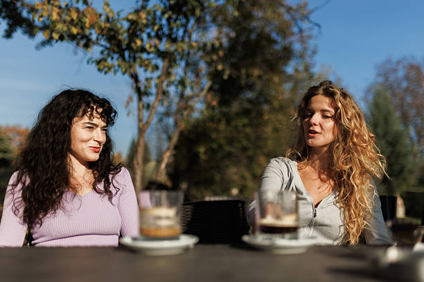 istock Two friends enjoying drinks outdoors on a sunny day with clear blue skies while engaging in conversation in a relaxed setting 2239754398