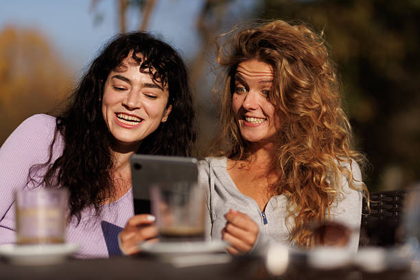 istock Two friends enjoying a sunny afternoon outdoors while sharing laughs and looking at a tablet in a relaxed setting with drinks nearby 2239754412