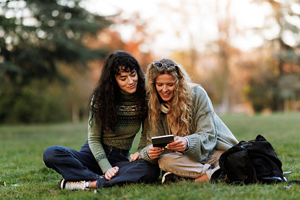 istock Friends enjoying time together in a park while sharing memories captured on a device during a sunny afternoon 2239754516