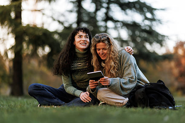 istock Two friends enjoying a sunny afternoon in the park while sharing a light moment and reading together on a green lawn surrounded by trees 2239754524