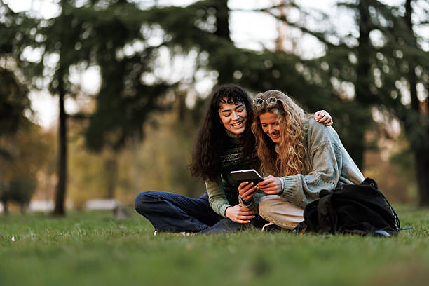 istock Two friends enjoying a relaxed moment while sharing a digital device in a sunny park during early evening hours 2239754541