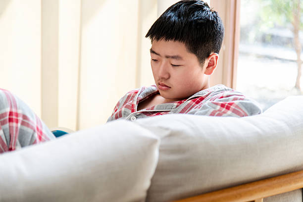 Teenage boy is reading book on sofa
