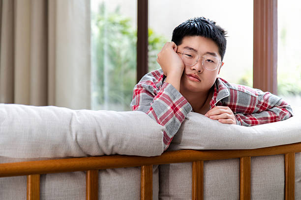 Sad teenage boy sitting on sofa and looking at camera