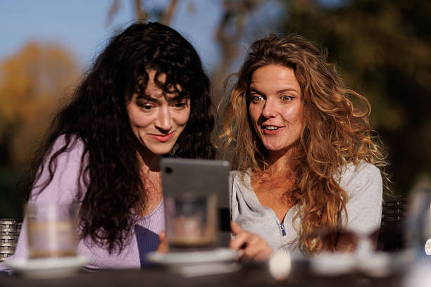 istock Two friends enjoying a sunny afternoon together while sharing joyful moments and laughter over a tablet at an outdoor cafÃ© 2239760672