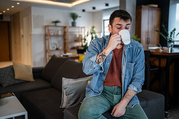 istock Tattooed man drinking coffee sitting on couch in living room 2239766169