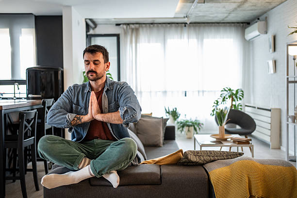 istock Man meditating in prayer hands position on couch at home 2239772584