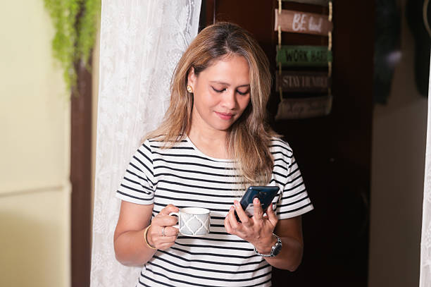 istock Smiling Woman Talking on Phone While Having Coffee at Home 2239773108