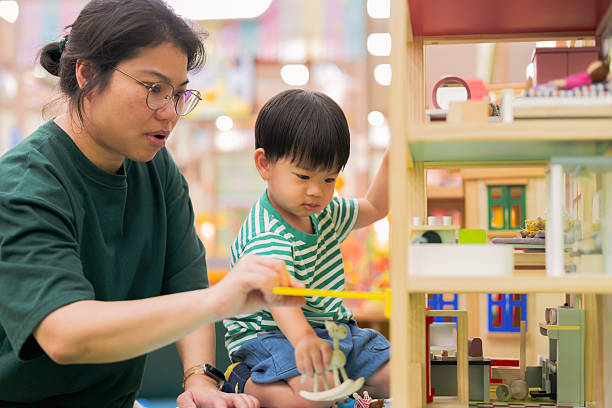 istock Cheerful mother takecare Asian boy develops cognitive skills and muscle coordination through playful exploration with colorful plastic toys at indoor playground, fostering brain development and creative problem solving abilities 2239777300