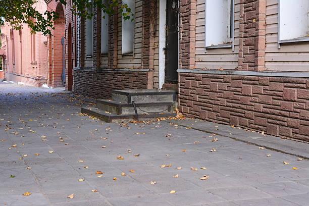Aged brick building with steps and sidewalk, autumn leaves scattered on the ground