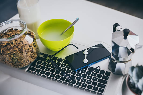 Table set for breakfast, kitchen in the background. Natural meal and technology devices. Interior view of a cozy and modern home. Millennial, youth, home working, home schooling, remote work concept.