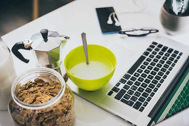 Table set for breakfast, kitchen in the background. Natural meal and technology devices. Interior view of a cozy and modern home. Millennial, youth, home working, home schooling, remote work concept.