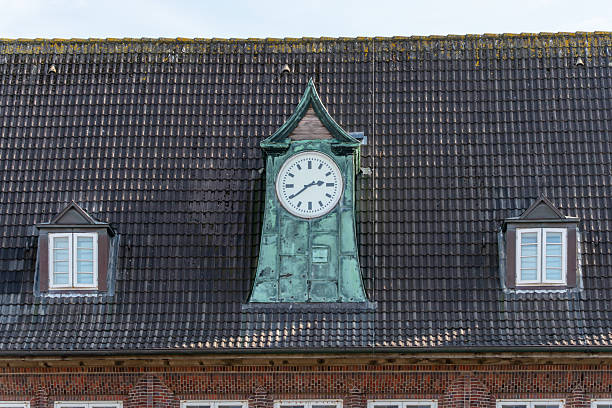 A green tower clock face sits atop a slate roof. Two small skylights flank the clock.