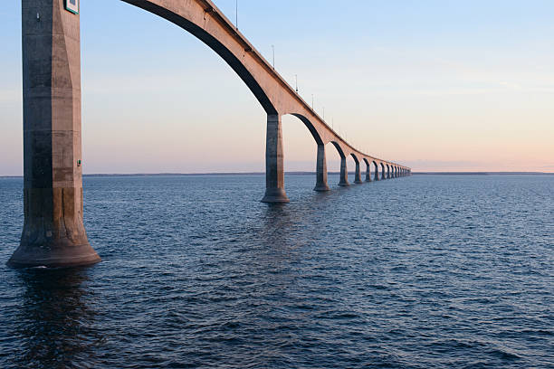 View of the Confederation Bridge extending across the Northumberland Strait between Prince Edward Island and New Brunswick, Canada. Captured at sunset, the image highlights the bridge's elegant concrete arches over calm blue water.