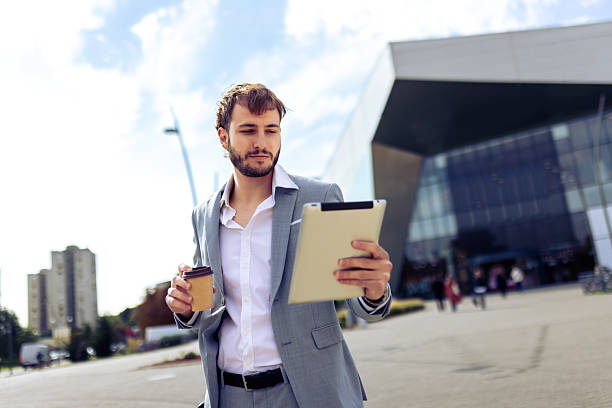 istock Businessman using tablet while holding coffee outdoors 2239792486