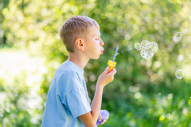 istock Teen boy blowing soap bubbles in summer park 2239793680