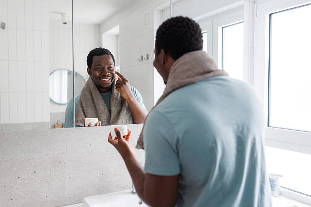 istock Young man applying face cream while looking in the mirror 2239797300