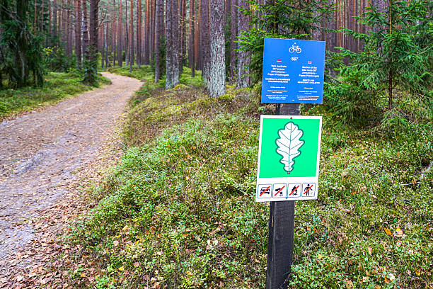 Signpost on a forest trail displays bicycle route info and oak leaf protected area sign with rules against driving, fires, and littering in nature reserve