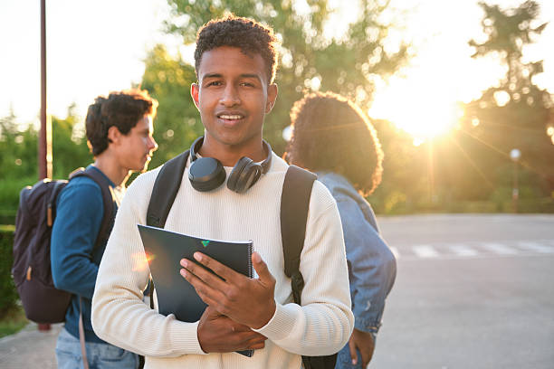 istock Smiling male student holding notebook on campus at sunset 2239802350
