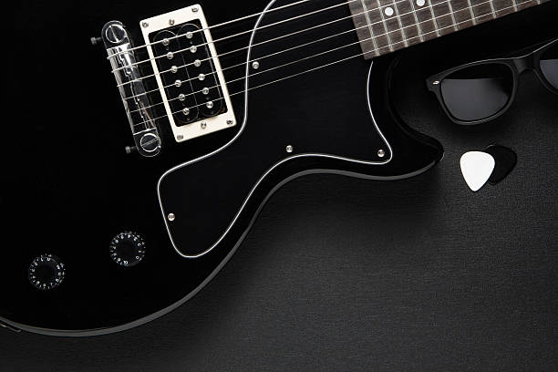Black electric guitar, sunglasses, and guitar picks on a textured dark background, top-down view.