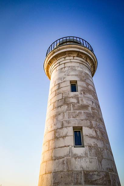 A low-angle view of a historic stone lighthouse against a clear blue sky.