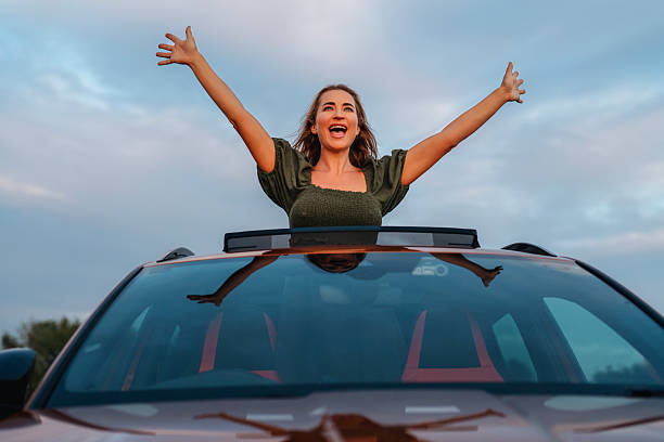 istock Joyful woman celebrates from car rooftop during sunset drive 2239807777