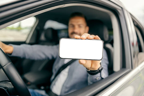 istock Man driving car showing smartphone blank screen mockup 2239811655