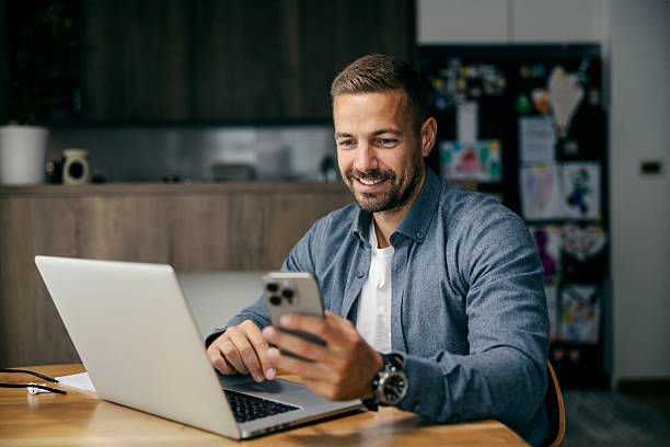 istock Smiling man using smartphone and laptop working from home 2239811743