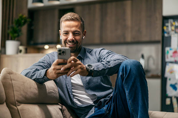 istock Man relaxing on couch using smartphone and earbuds 2239811781