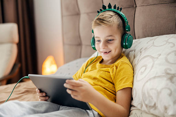 istock Boy using digital tablet with headphones in bed 2239814541