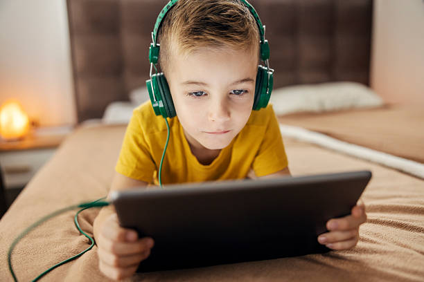 istock Boy wearing headphones using digital tablet in bed 2239814591