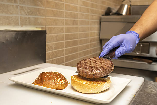 istock A chef with a gloved hand assembling a freshly cooked burger on top of a toasted muffin 2239817849