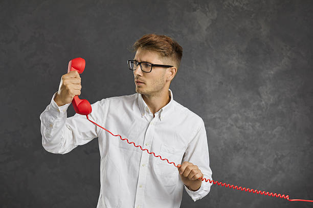 Millennial man talk on corded telephone on black background