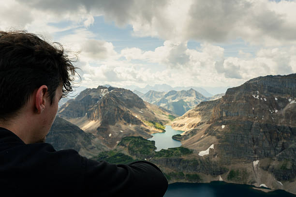 istock Man views mountain vista towering peaks and tranquil blue lakes below. 2239825038