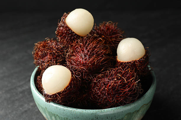 Delicious ripe rambutans in bowl on black table, closeup