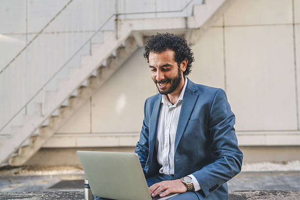 istock Smiling businessman working on laptop outdoors in urban setting 2239830998