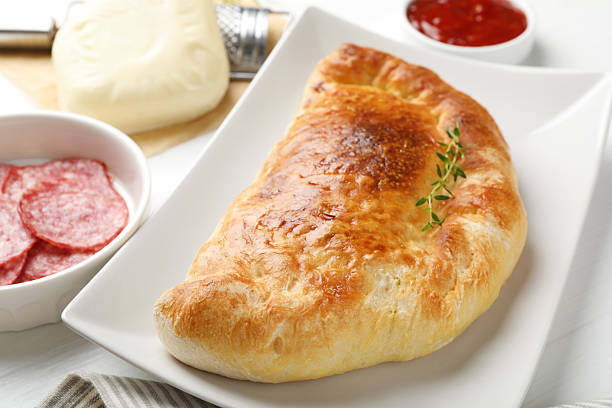 Delicious fresh calzone pizza and ingredients on white table, closeup
