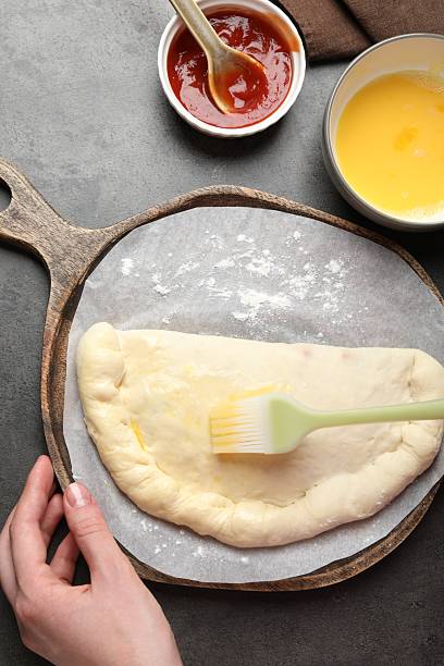 istock Woman brushing egg yolk on calzone pizza at grey table, top view 2239833619