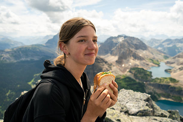 Woman enjoying a sandwich with mountain view. Outdoor meal at scenic peak.