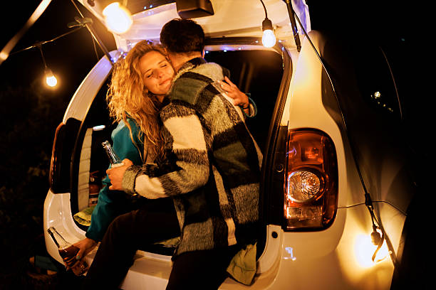 istock Young couple enjoying a cozy evening by their car while sharing drinks and a warm embrace under string lights at night 2239843623