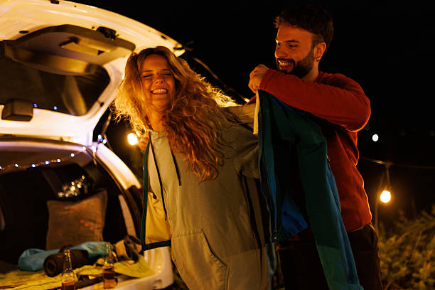 Friends enjoying a fun night outdoors while preparing for a camping adventure under the stars at a cozy campsite with lights in the background