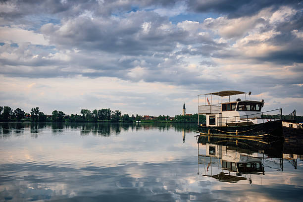 istock Old river ships under the Serbian flag, standing on a pier on the Danube against a cloudy sky and an old bell tower 2239853366